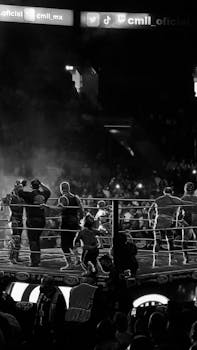 Energetic black-and-white shot of a boxing match in an arena with a lively crowd in Ciudad de México.
