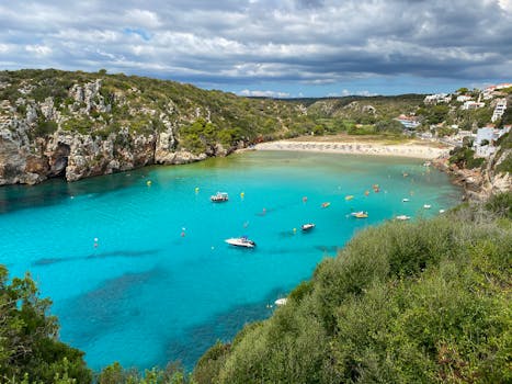 Stunning aerial shot of the vibrant Cala en Porter beach in Menorca, showcasing turquoise waters and rugged cliffs.