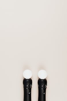 Vertical overhead shot of two black gaming controllers with circular sensors, set against a neutral background. Ideal for tech and gaming concepts.